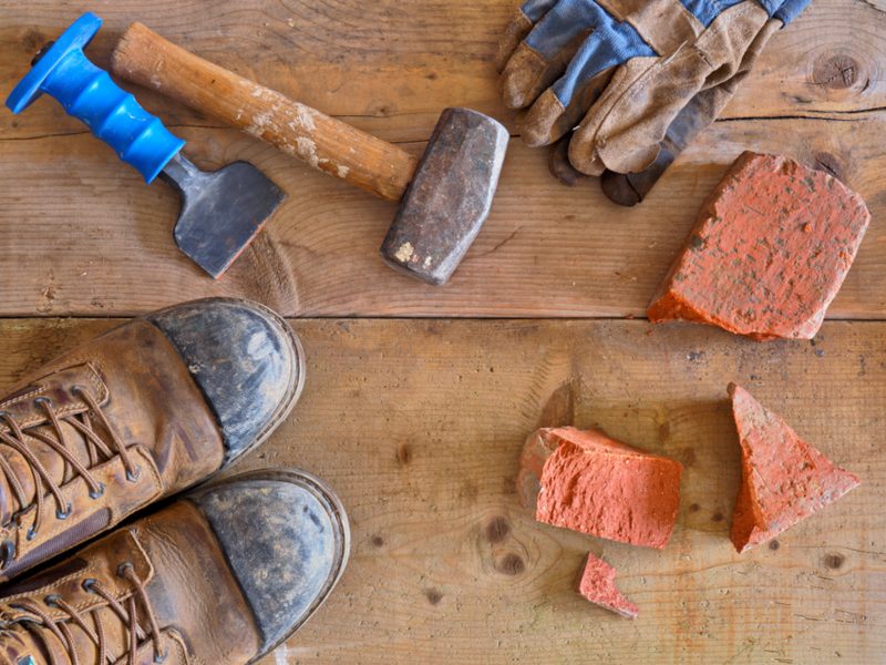 Massette, burin, gants et briques posés sur un plancher de chantier