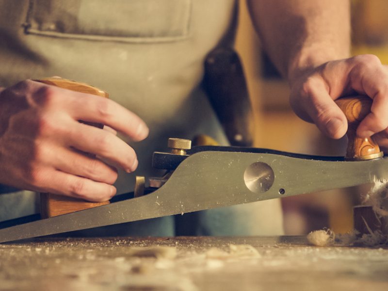 Mains d'artisan guidant un rabot sur une pièce de bois